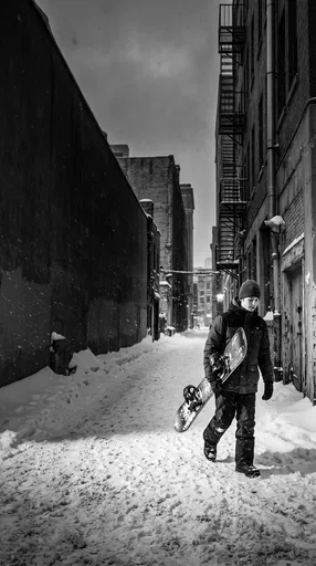 Teenage Boy With Snowboard in Snowy Alley
