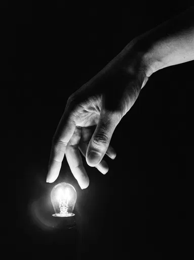 Hand Hovering Over Glowing Filament Bulb