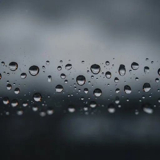 Raindrops on Window Against Grey Sky