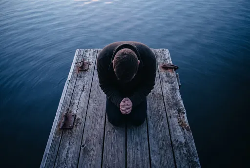 Person Kneeling in Prayer on Wooden Dock