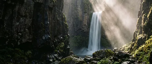 Sunlit Waterfall in Dark Rocky Canyon